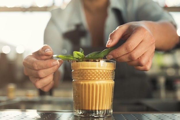 Nahaufnahme von weiblichen Händen, die leckeren alkoholfreien Cocktail mit kaltem Kaffee mit Minze vorbereiten und servieren. Barkeeper an seinem Arbeitsplatz. Kleinunternehmenskonzept, Kopienraum