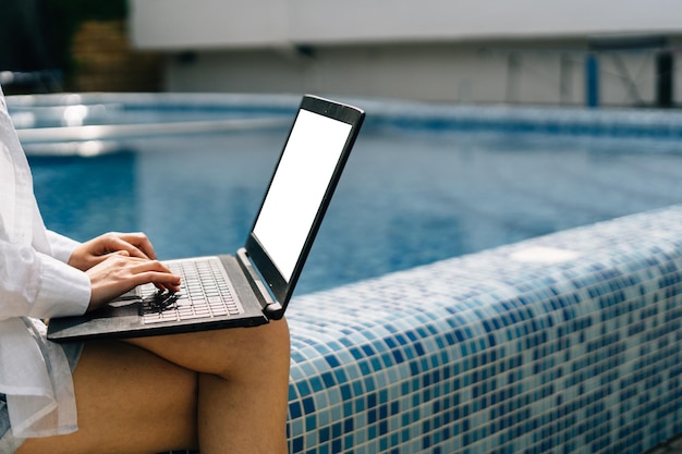 Nahaufnahme von weiblichen Händen tippen Text auf der Laptop-Tastatur Remote-Arbeit im Urlaub am Pool Weißer leerer Notebook-Bildschirm Remote-Arbeitskonzept