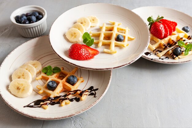 Nahaufnahme von weichen Wiener Waffeln auf den drei Tellern mit Heidelbeeren-, Erdbeer- und Schokoladensauce