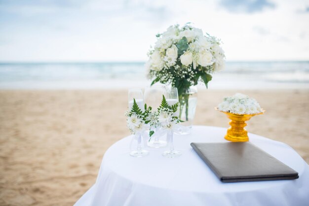 Nahaufnahme von weißen Blumen und Weingläsern auf einem Tisch am Strand
