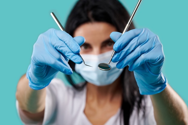 Nahaufnahme von zahnärztlichen Metallwerkzeugen in den Händen der Zahnarztfrau auf einem blauen Hintergrund