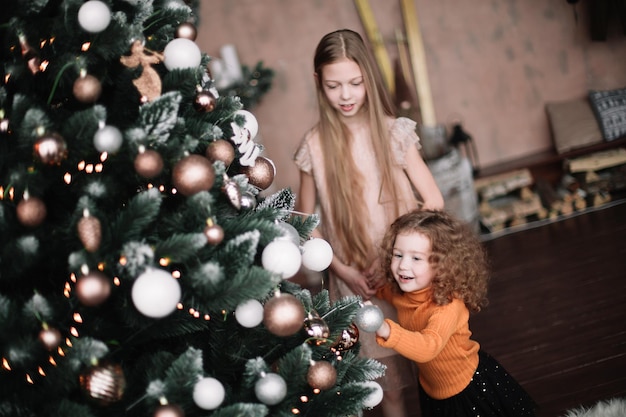 Nahaufnahme von zwei hübschen Schwestern, die am Weihnachtsbaum stehen