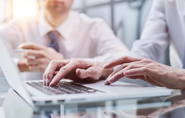 Nahaufnahme von zwei jungen Kollegen, die im Büro an einem mobilen Laptop-Computer arbeiten