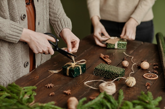 Nahaufnahme von zwei nicht erkennbaren Frauen, die Weihnachtsgeschenke im rustikalen Holztisch-Kopierraum verpacken