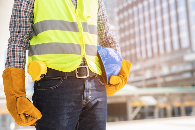 Nahaufnahme Vorderansicht Ingenieur männlicher Bauarbeiter stehen halten Sicherheit blauen Helm und tragen Handschuhe mit reflektierender Kleidung