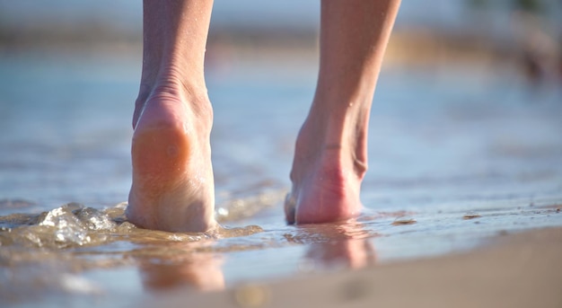 Nahaufnahme weiblicher Füße, die barfuß auf weißem, körnigem Sand des goldenen Strandes auf blauem Ozeanwasserhintergrund laufen