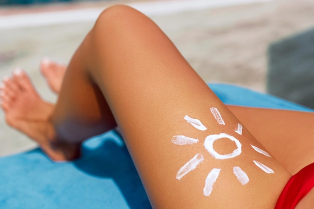 Nahaufnahme weibliches Bein mit Sonnenform Sonnencreme Sonnencreme auf ihren glatten gebräunten Beinen Sonnencreme