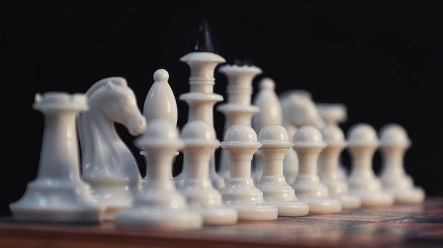 Nahaufnahme weißer Schachfiguren entlang des Bretts gegen einen dunklen Hintergrund in diagonaler Anordnung