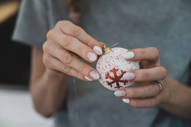 Nahaufnahmeansicht der weiblichen Hände mit der Winterferienmaniküre, die einen dekorativen Weihnachtsflitter hält.