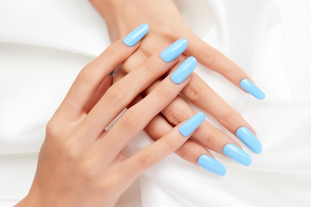 Nahaufnahmeaufnahme der Hände einer Frau mit blauem Nagellack auf einem weißen Seidenstoff
