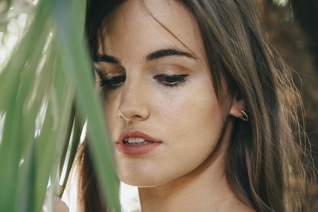 Nahaufnahmeaufnahme eines attraktiven brünetten Mädchens mit einer perfekten Haut nahe der grünen Pflanze