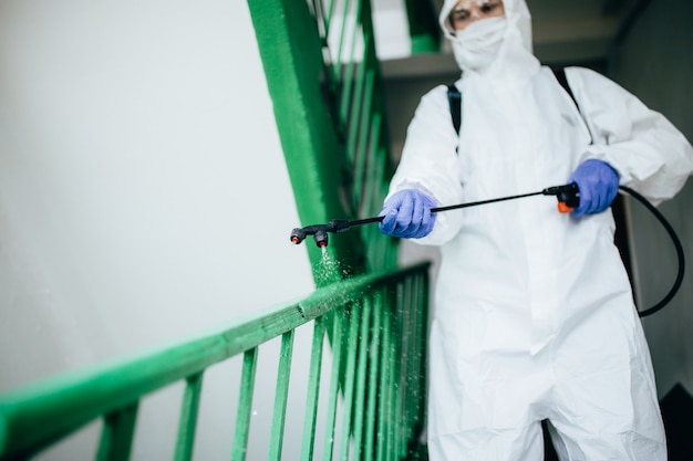 Nahaufnahmeaufnahme eines sanitären professionellen Arbeiters, der Schutzanzug desinfiziert, der einen Treppenhaus-Eingangsblock von Wohnungen desinfiziert. Coronavirus-Prävention in Wohnbereichen. Neue Normal- und Stopp-Covid-19-Ausbreitung.