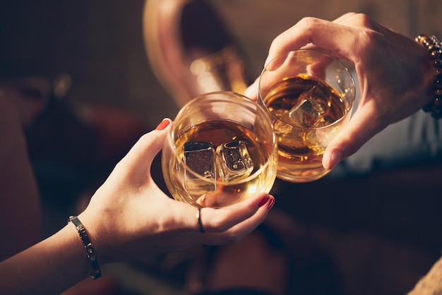 Nahaufnahmeaufnahme von zwei Personen, die Gläser mit Alkohol an einem Toast anstoßen
