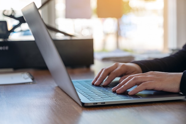 Nahaufnahmebild der Hände, die Laptop-Tastatur auf Holztisch im Büro verwenden und tippen