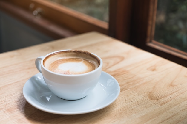 Nahaufnahmebild der heißen Kaffeetasse auf Weinlese-Holztisch im Café