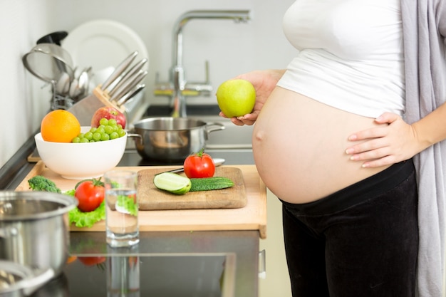 Nahaufnahmebild der schwangeren Frau, die Abendessen in der Küche kocht