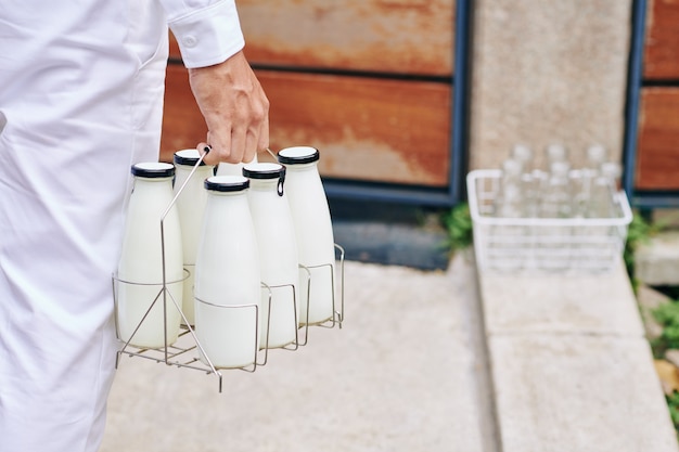 Nahaufnahmebild des Auslieferungsmannes, der Flaschen der frischen Milch zur Eingangstür trägt
