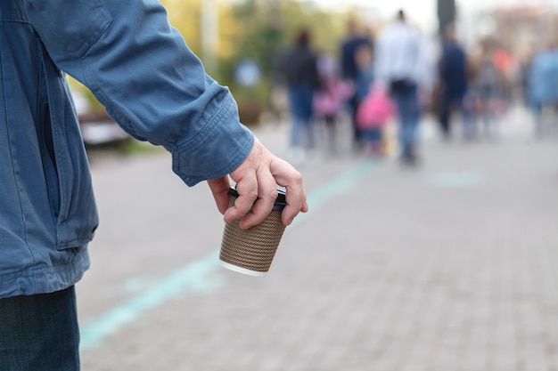 Nahaufnahmebild des jungen Hipster-Mannes, der Stadtstraßen geht und Kaffee trinkt, um nach draußen zu gehen, Mann, der lässigen Hoodie trägt und seinen Cappuccino genießt