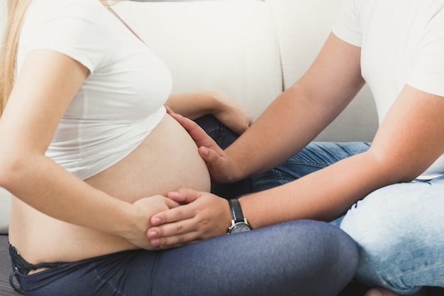 Nahaufnahmebild des jungen Paares, das Baby erwartet. Mann hält Händchen am dicken Bauch