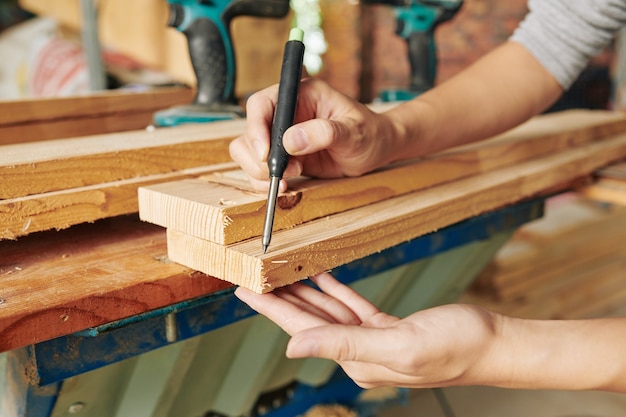 Nahaufnahmebild des Zimmermanns, der Markierungen auf langem Holzbrett zeichnet, bevor es schneidet und Möbeleinheit macht