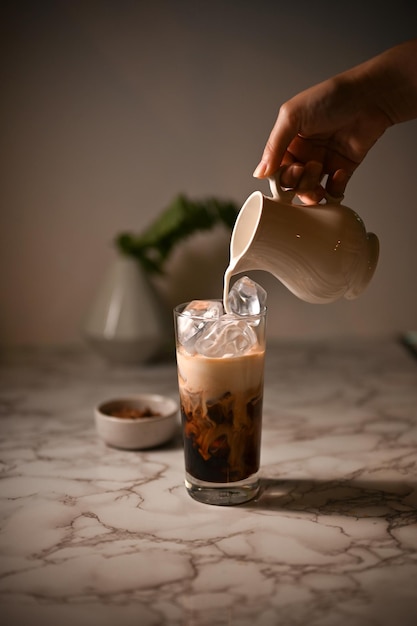 Nahaufnahmebild Die Hand der weiblichen Barista gießt eine frische Milch in ein Glas Eiskaffee