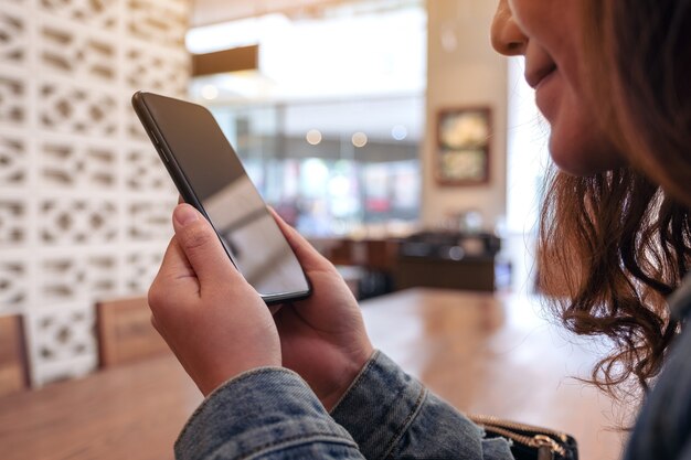 Nahaufnahmebild einer asiatischen frau, die das smartphone im café hält, benutzt und betrachtet