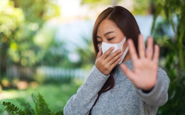 Nahaufnahmebild einer asiatischen frau, die eine schützende gesichtsmaske trägt, die das stopphandzeichen zur Verhinderung der Ausbreitung von Covid-19 zum Pandemiekonzept macht