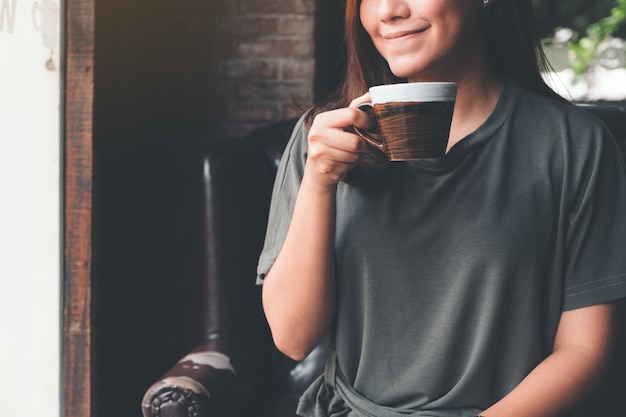 Nahaufnahmebild einer asiatischen Frau, die heißen Kaffee mit dem guten Gefühl im Weinlesecafé hält und trinkt