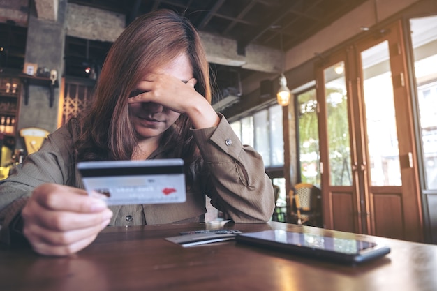 Nahaufnahmebild einer asiatischen Frau, die Kreditkarte mit dem Gefühl gestresst und gebrochen, Handy auf dem Tisch hält