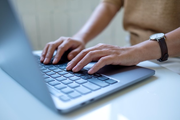 Nahaufnahmebild einer Frau, die auf der Tastatur eines Laptops auf dem Tisch arbeitet und tippt