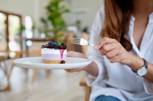 Nahaufnahmebild einer Frau, die ein Stück Blaubeerkäsekuchen hält und isst