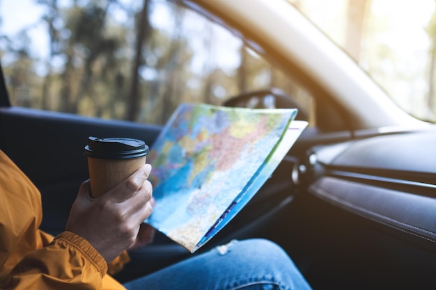 Nahaufnahmebild einer Frau, die eine Karte für Richtung liest und Kaffee im Auto trinkt