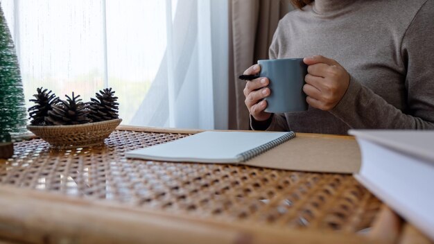 Nahaufnahmebild einer Frau, die Kaffee hält und trinkt, während sie zu Hause lernt