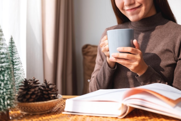 Nahaufnahmebild einer Frau, die Kaffee trinkt, während sie zu Hause ein Buch liest