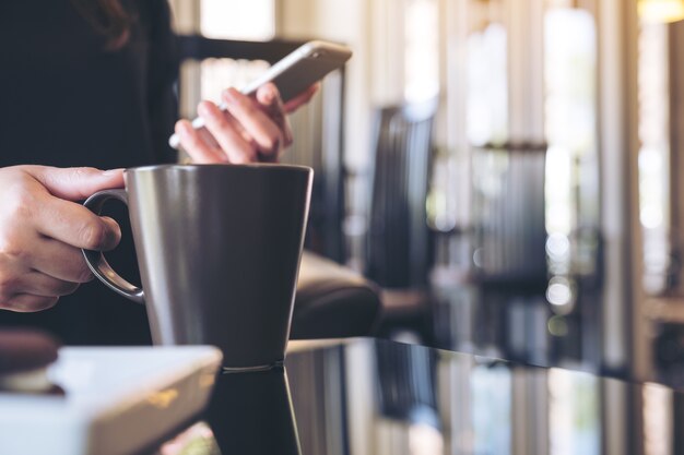 Nahaufnahmebild einer Frau, die Smartphone beim Trinken des Kaffees im Café hält und verwendet