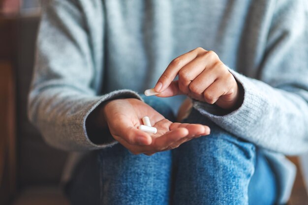 Nahaufnahmebild einer Frau, die weiße Medizinkapseln in der Hand hält und auswählt