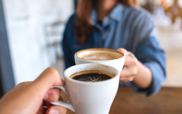 Nahaufnahmebild einer Frau und eines Mannes, die zusammen Kaffeetassen im Café klirren