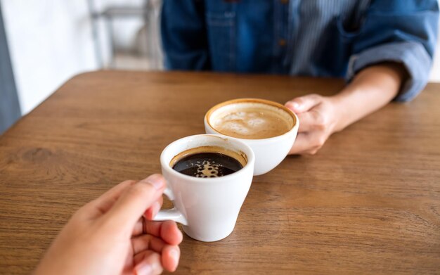 Nahaufnahmebild einer Frau und eines Mannes, die zusammen Kaffeetassen im Café klirren