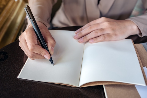 Nahaufnahmebild einer Geschäftsfrau, die auf leerem Notizbuch auf Holztisch schreibt