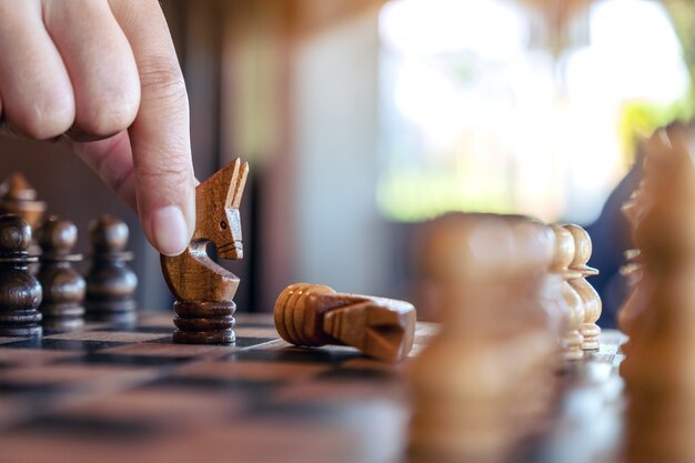 Nahaufnahmebild einer Hand, die ein Pferd hält und bewegt, um ein anderes Pferd im hölzernen Schachbrettspiel zu gewinnen