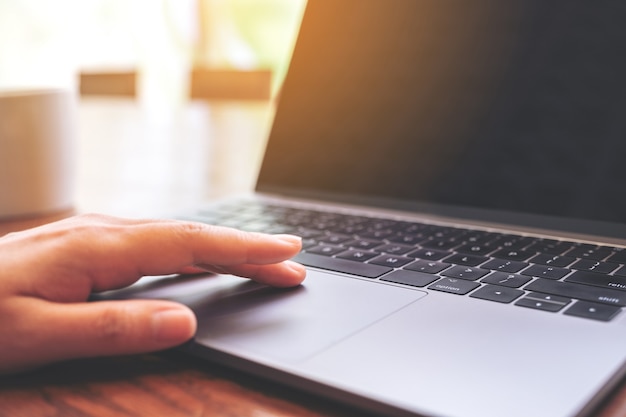 Nahaufnahmebild einer Hand, die Laptop-Touchpad mit Kaffeetasse auf Holztisch verwendet und berührt