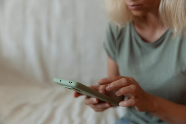 Nahaufnahmebild einer hübschen Frau, die in einem gemütlichen Zuhause sitzt und mit weiblichen Händen eines modernen Smartphone-Geräts eine Textnachricht über das soziale Netzwerkkonzept des Mobiltelefons eingibt