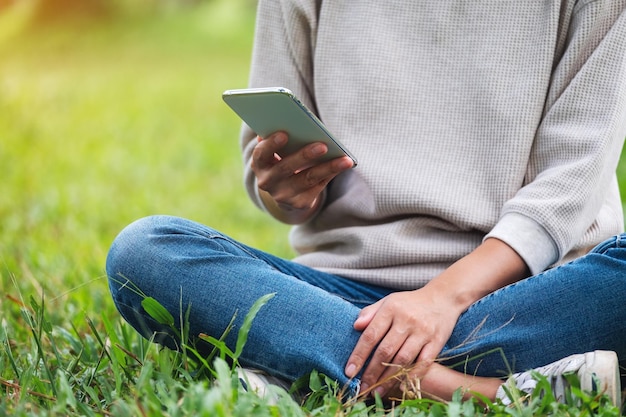 Nahaufnahmebild einer jungen Frau, die Handy im Park hält und verwendet