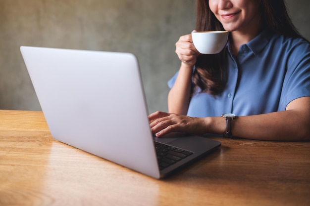 Nahaufnahmebild einer jungen Frau, die Kaffee trinkt, während sie an einem Laptop arbeitet