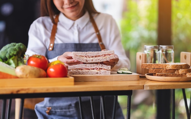 Nahaufnahmebild einer Köchin, die ein Stück Vollkornschinken-Käse-Sandwich in der Küche kocht und hält