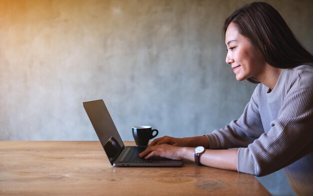 Nahaufnahmebild einer schönen asiatischen Frau, die auf der Tastatur eines Laptops auf dem Tisch arbeitet und tippt