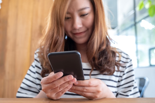 Nahaufnahmebild einer schönen asiatischen Frau, die das Smartphone im Café hält, benutzt und betrachtet