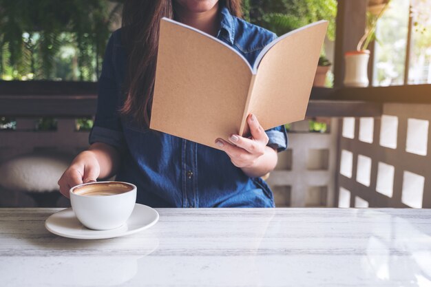 Nahaufnahmebild einer schönen asiatischen Frau, die ein Buch beim Kaffeetrinken im modernen Café liest