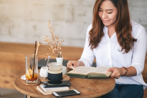 Nahaufnahmebild einer schönen asiatischen frau, die ein buch hält und liest, während sie im café sitzt