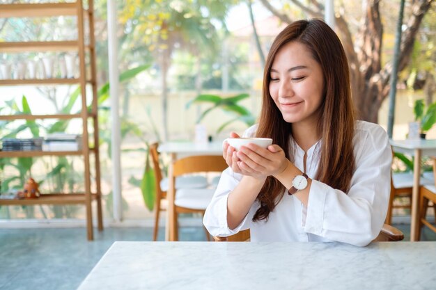 Nahaufnahmebild einer schönen asiatischen frau, die eine tasse heißen kaffees hält